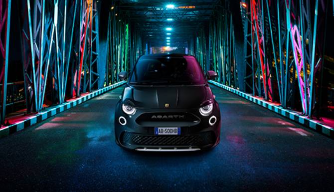 Black car on an illuminated bridge at night, viewed from the front.