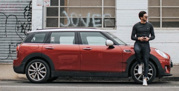 Man leaning on a red Mini parked on the street.