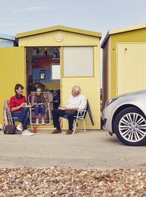 people sat outside of yellow hut with a car parked