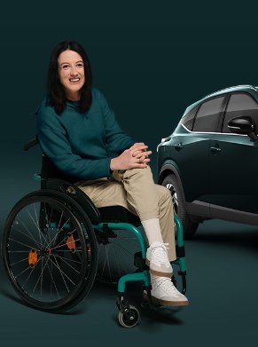 Woman in a wheelchair smiling next to a dark green SUV.