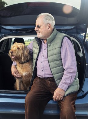 man sat on the boot of the car with his dog