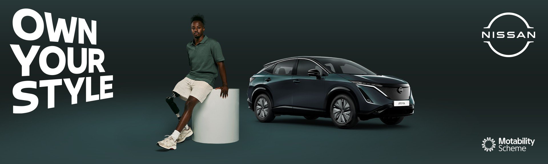 Man with a prosthetic leg sits on a stool next to a Nissan Ariya car.