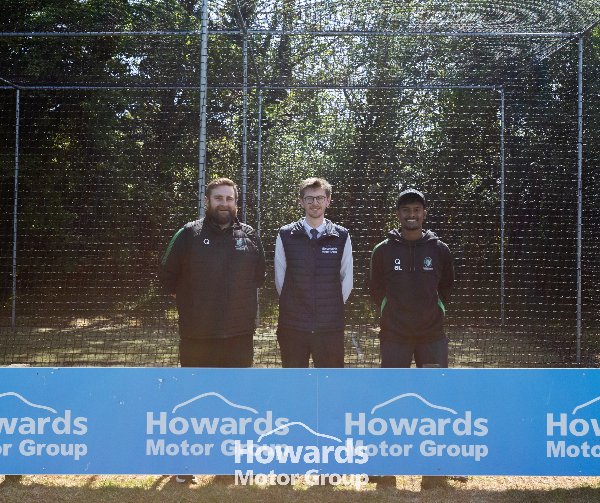 Three people standing in front of a cricket net next to a Howards Motor Group sign.