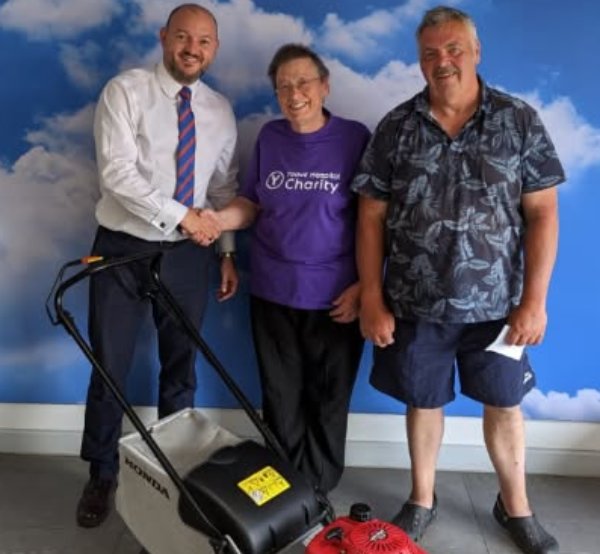 Three people standing with a lawnmower, one holding a piece of paper.