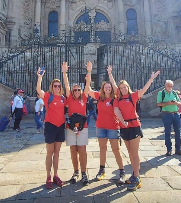 Four people in red shirts posing in front of a large historic building.