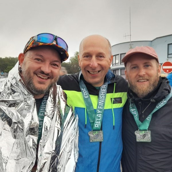 Three men wearing relay medals and smiling at a sports event.