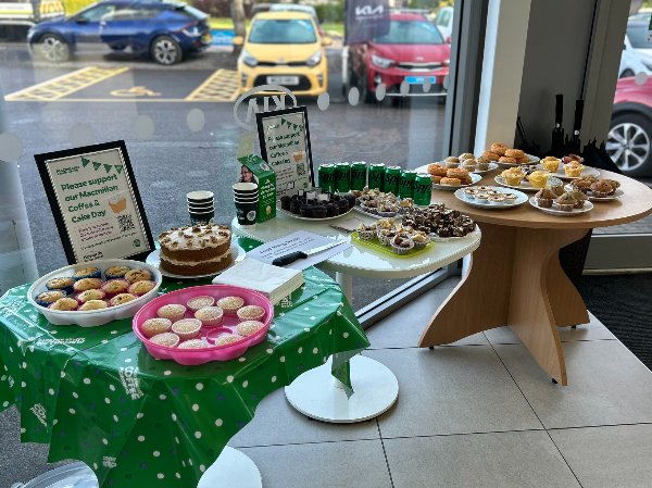 Tables with cakes, pastries, drinks, and signs for Macmillan Coffee and Cake Day fundraiser.