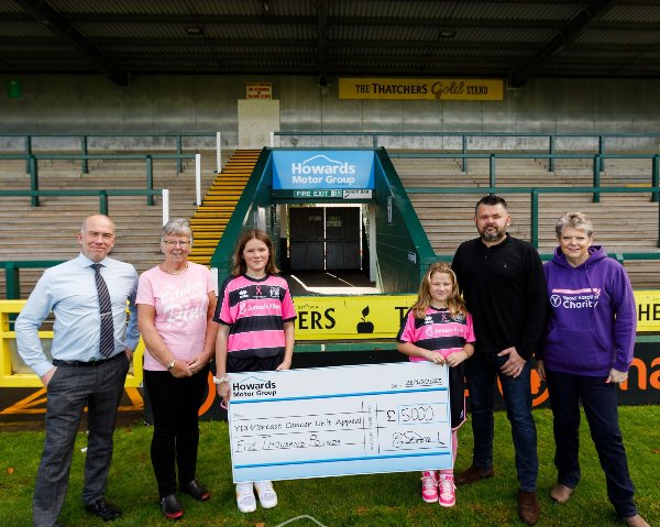 Group holding a large cheque for £5,000 charity donation at a stadium.