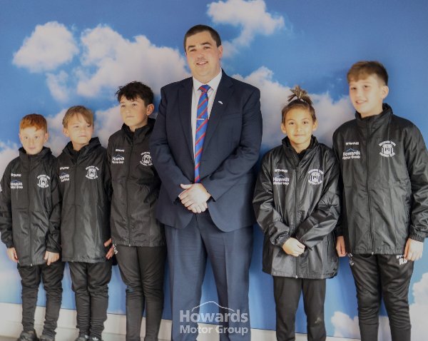 Seven people, including a man in a suit and six children in black sports jackets.