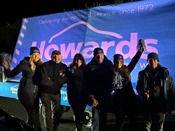 Six people in front of a large banner with the text Howards visible in blue and pink.