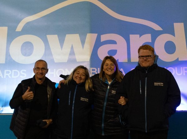 Four people in Howards Motor Group jackets smiling in front of a large branded sign.
