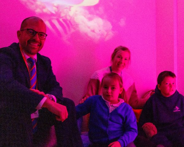 Four people sitting together in a room lit with pink light.
