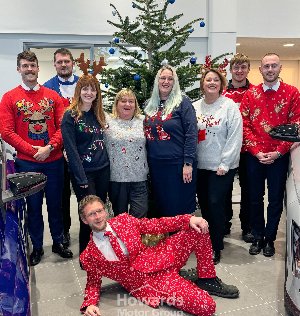 A group of nine people in festive jumpers and one lying down in a patterned red suit.