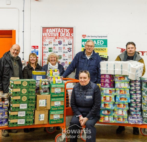 People posing with stacked food boxes and toiletries on a trolley.