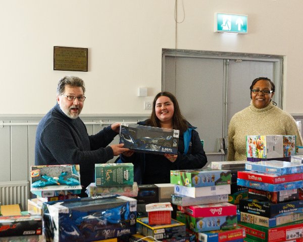 Three people stand behind stacks of board games.