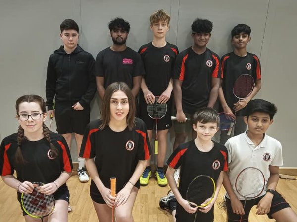 A group of young badminton players posing indoors with rackets.