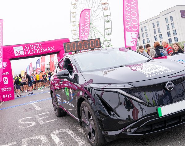 Black car at race start line with pink banners and Ferris wheel in background.