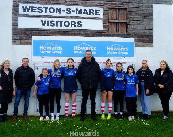 Group of people standing by a Weston-S-Mare sign at Howards Motor Group sports area.