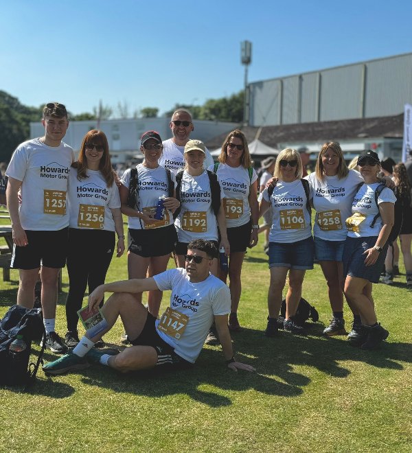 Group of people wearing matching event shirts and numbered bibs on grass.