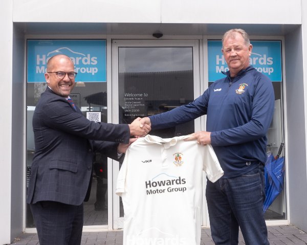 Two men shaking hands, holding a jersey outside Howards Motor Group entrance.