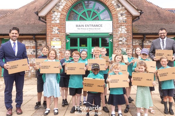 Children and two adults holding Asus boxes outside a school entrance.