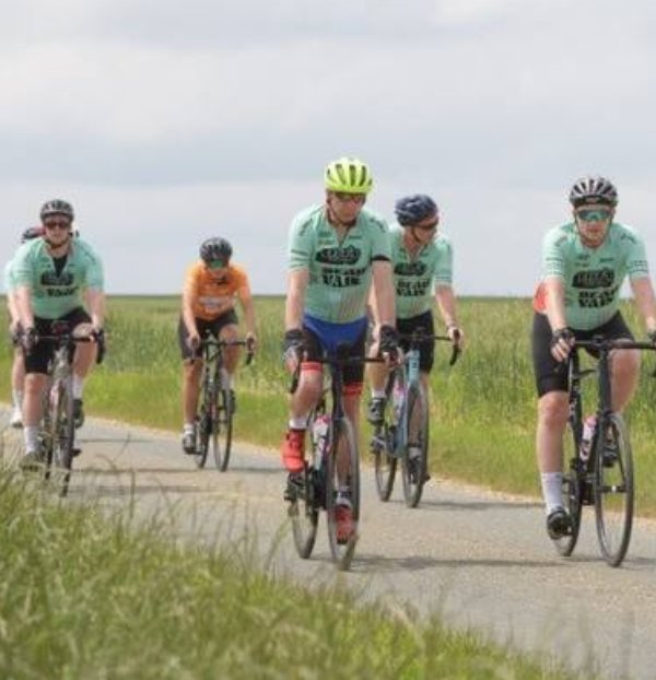 Group of cyclists riding on a rural road in matching green jerseys.