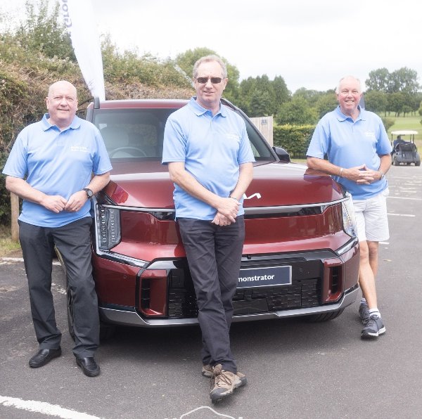 Three men in blue shirts standing in front of a maroon car marked as demonstrator.