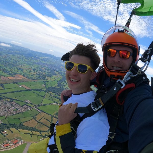 Tandem skydivers in mid-air above the countryside, smiling at the camera.