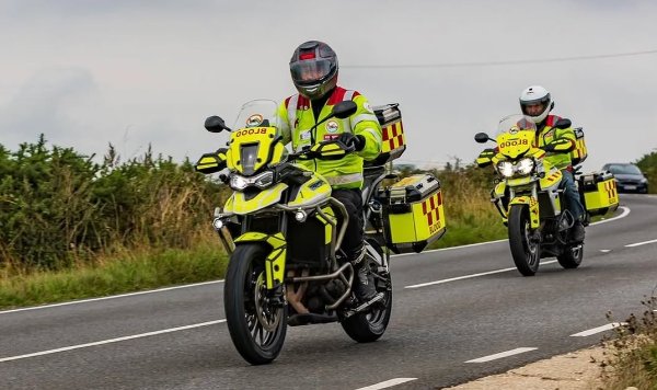 Motorcycle blood delivery riders in high-visibility gear on a rural road.