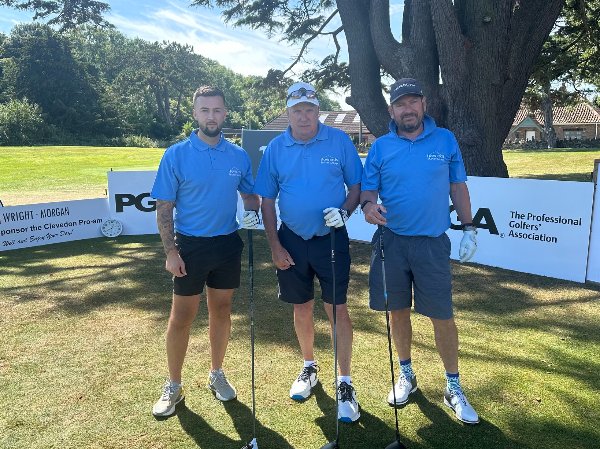 Three men in blue shirts holding golf clubs on a golf course during an event.
