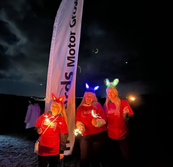 Three people in red shirts hold sparklers at night, wearing light-up headbands.
