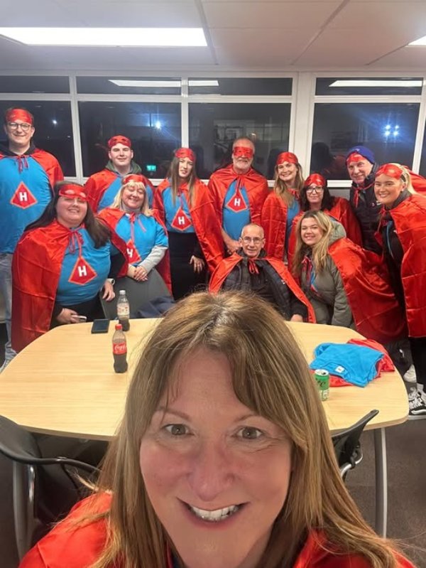 Group of people wearing red capes and masks around a table.