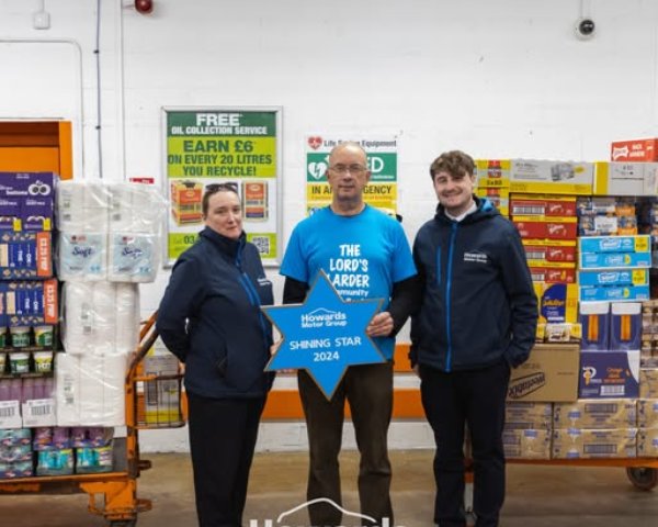 Three people stand with a Shining Star 2024 award in front of shelves stocked with household items.