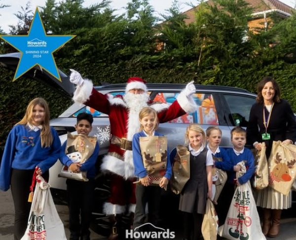 Santa Claus with a group of smiling children and an adult, holding gift bags by a car.