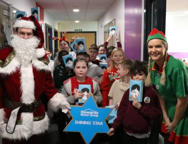 Santa and a group of children holding booklets, with an elf standing on the right.