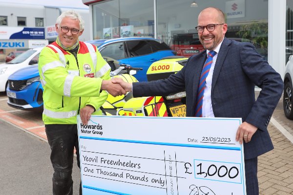 Two men shaking hands while holding a cheque for £1,000 to Yeovil Freewheelers.