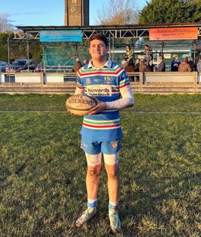 Rugby player in a striped kit holding a rugby ball on a grassy field.