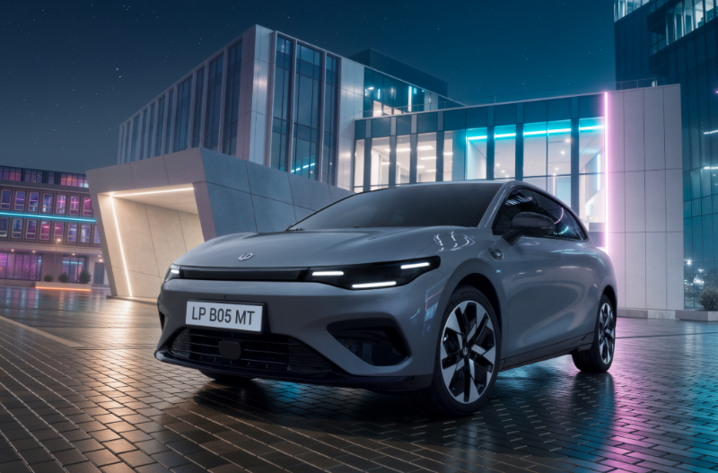 A silver electric car parked near modern buildings at night.