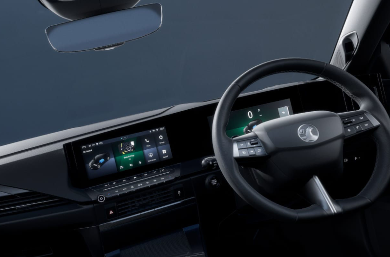 Car interior showing steering wheel and digital dashboard display.