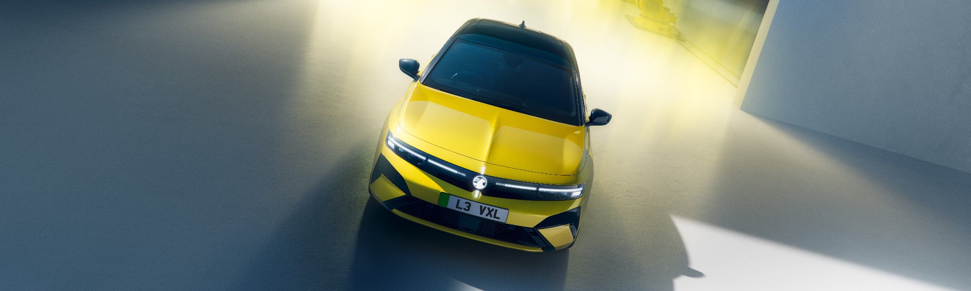 A yellow car with L3 VXL number plate in front of robotic arms and a yellow light.
