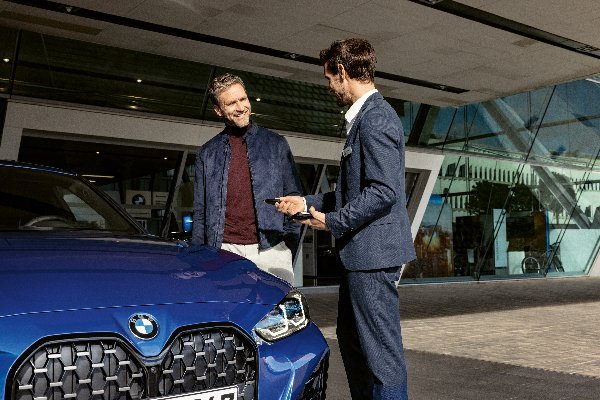 Two men standing beside a blue BMW car, one holding a tablet.
