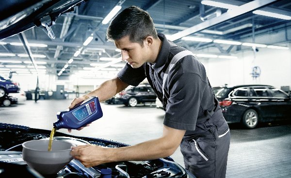 Mechanic pouring motor oil into a car engine with a funnel in a garage.
