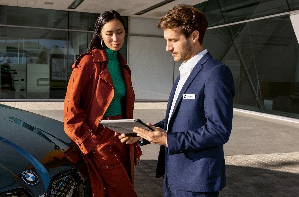 A man and woman standing next to a car, looking at a tablet.
