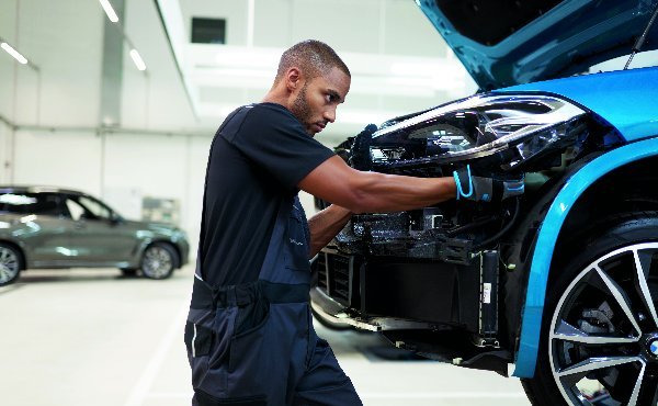 Mechanic repairing the front of a blue car in a workshop.
