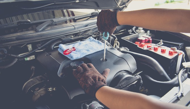 Mechanic's gloved hands using a screwdriver on a car engine.