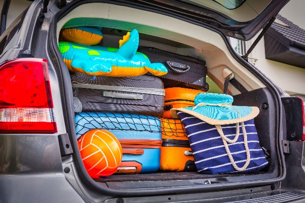 Car boot packed with suitcases, an inflatable toy, beach bag, and ball.