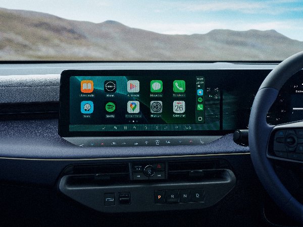 Car dashboard with digital display showing app icons and steering wheel on the right.