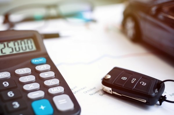Calculator and car key on paper, with blurred car and glasses in the background.
