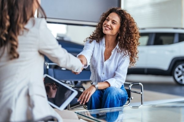 Two people shaking hands in an office setting, one holding a tablet.