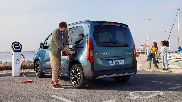 car parked by harbour. Man charging car, children stand nearby